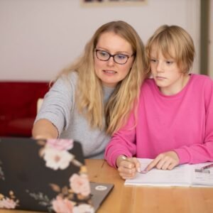Mother assisting her child with homework at a laptop while reviewing 8th grade math standards together at home.