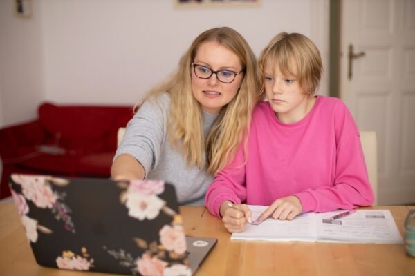 Mother assisting her child with homework at a laptop while reviewing 8th grade math standards together at home.