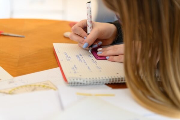 Close-up of a student using a ruler and notebook for geometry problem solving at a desk.