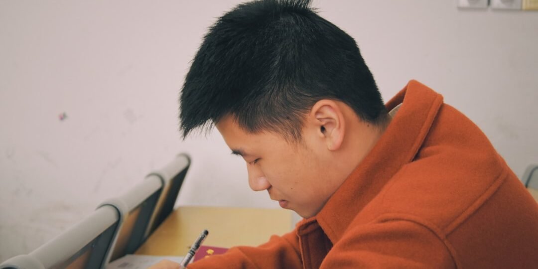 A student in an orange coat writes on a piece of paper. Many students find the psat is easier than the sat.