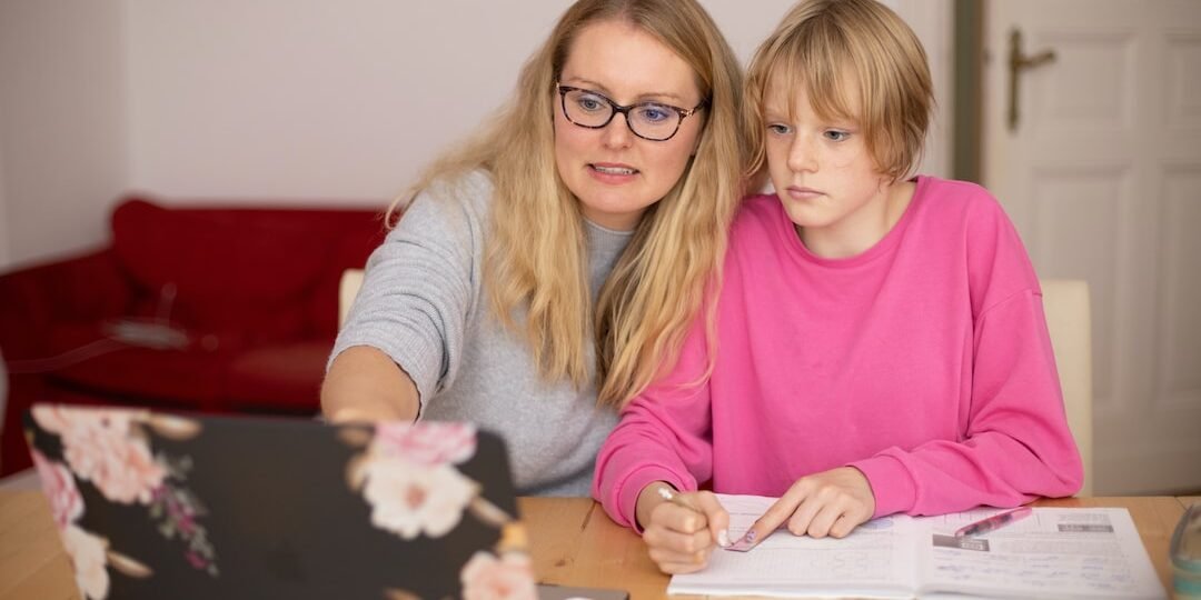 Mother assisting her child with homework at a laptop while reviewing 8th grade math standards together at home.