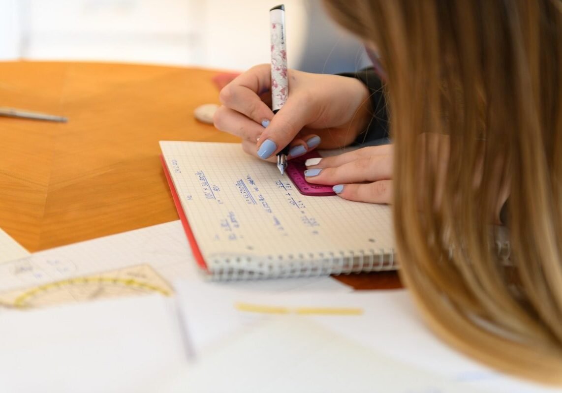 Close-up of a student using a ruler and notebook for geometry problem solving at a desk.