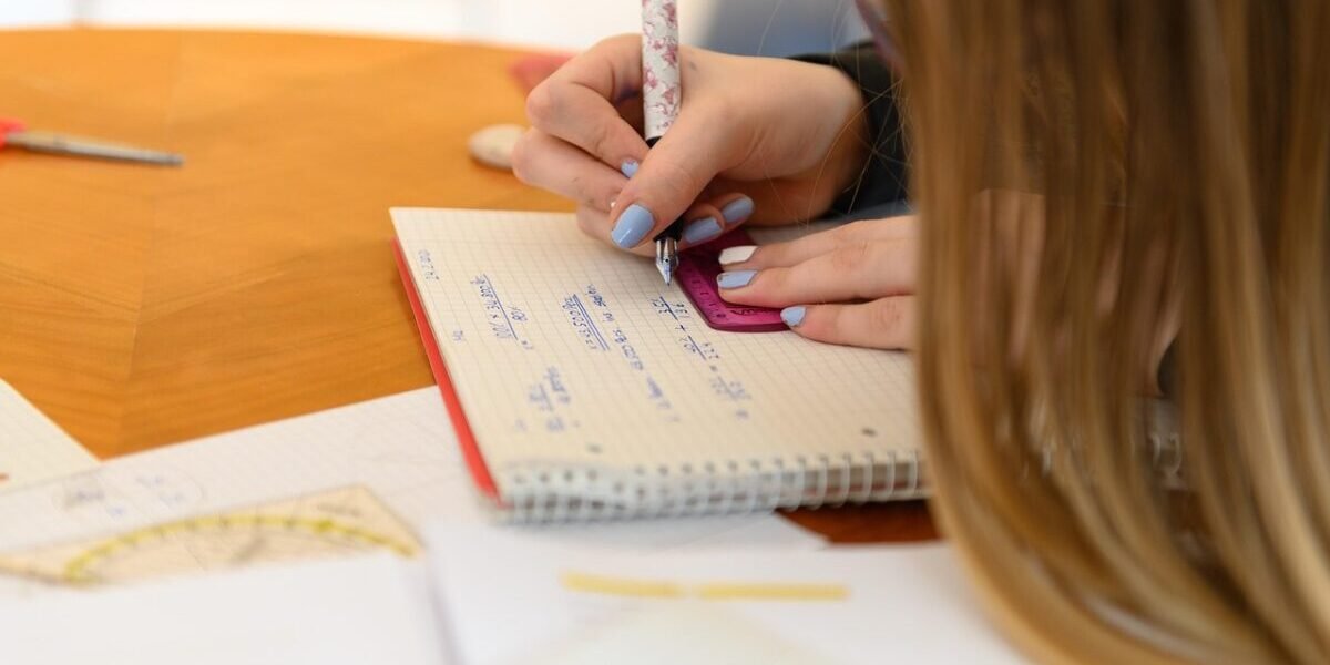 Close-up of a student using a ruler and notebook for geometry problem solving at a desk.