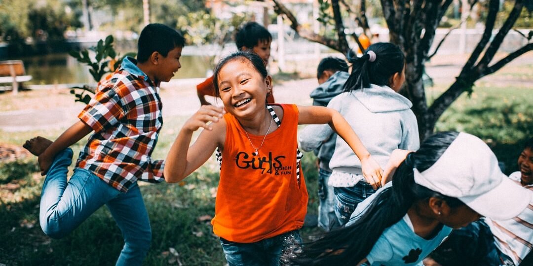 A group of four boys and three girls are smiling and playing outside