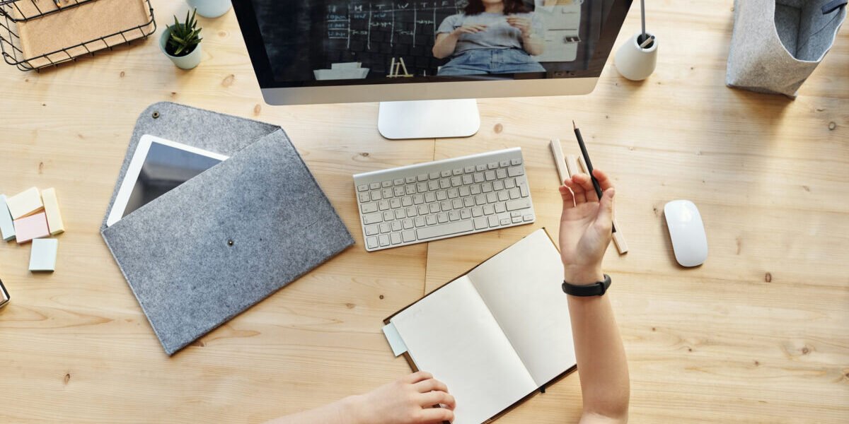 Kids hands with pencil and notebook on a desk attending a virtual class