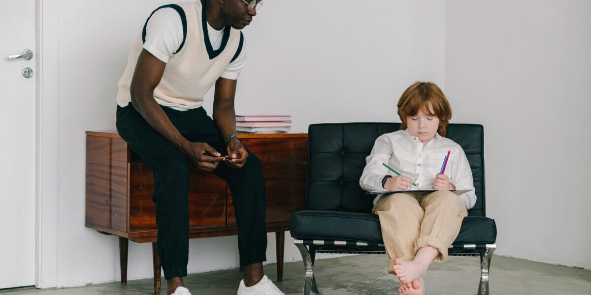 Tutor guiding kid working sitting on a chair